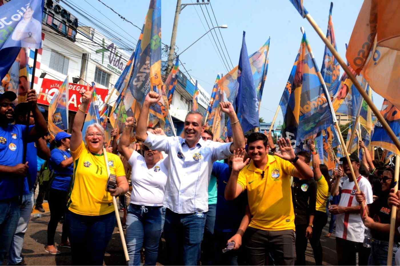 Professor Rodolfo lidera caminhada ao lado de apoiadores com bandeiras erguidas, durante evento em Várzea Paulista