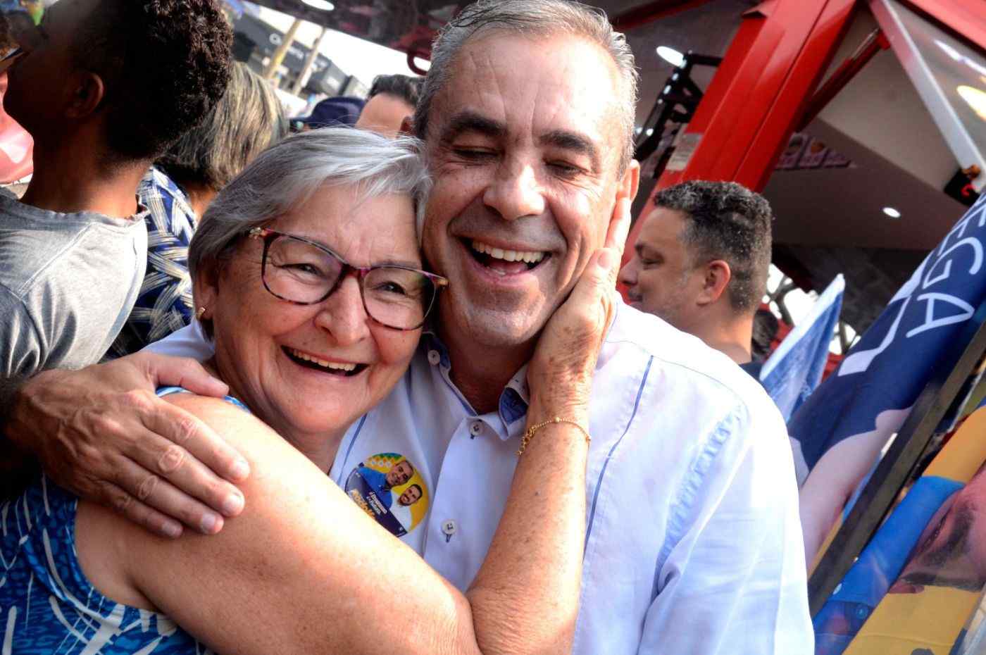 Professor Rodolfo abraça apoiadora sorridente durante evento público em Várzea Paulista, transmitindo simpatia e proximidade