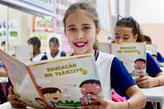 Aluna olha para a câmera segurando livro do programa em sala de aula