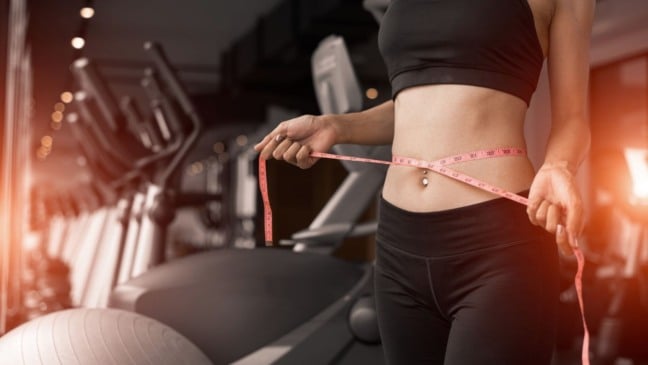 Mulher medindo a cintura com fita métrica em academia