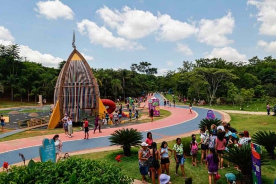 Vista ampla do parque Mundo das Crianças, em Jundiaí, em um dia ensolarado, com famílias e crianças aproveitando as atrações ao ar livre. Em destaque, a estrutura em formato de foguete, pista colorida para caminhada e áreas verdes ao redor.