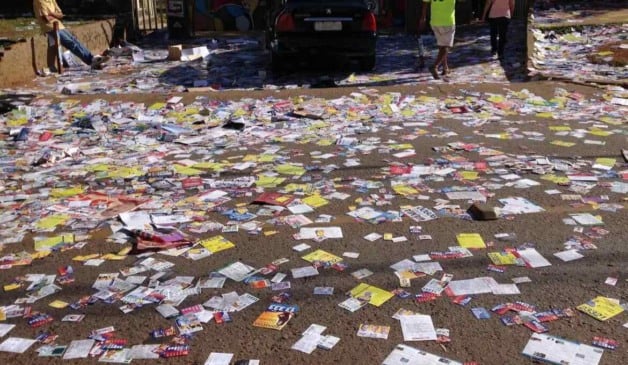 Ruas cobertas de panfletos de propaganda eleitoral, evidenciando poluição visual e excesso de material de campanha.