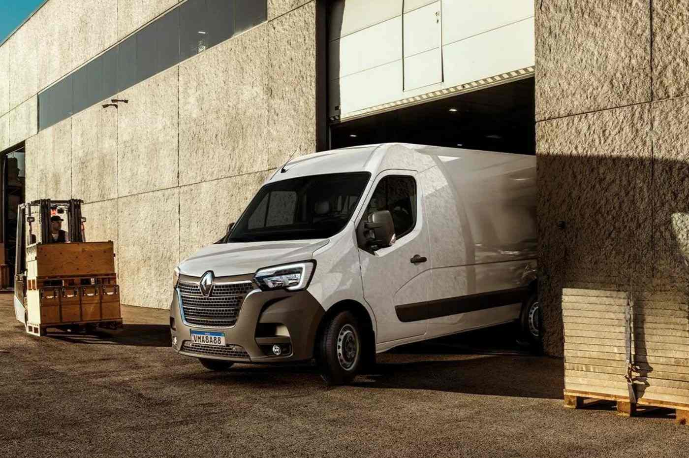 Renault Master branca saindo de doca de carga, ideal para logística e transporte urbano, ao lado de empilhadeira em operação.