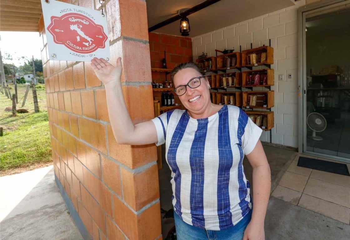 Mulher sorridente em frente a placa da Rota Turística Cultura Italiana em Jundiaí, promovendo o turismo rural na região
