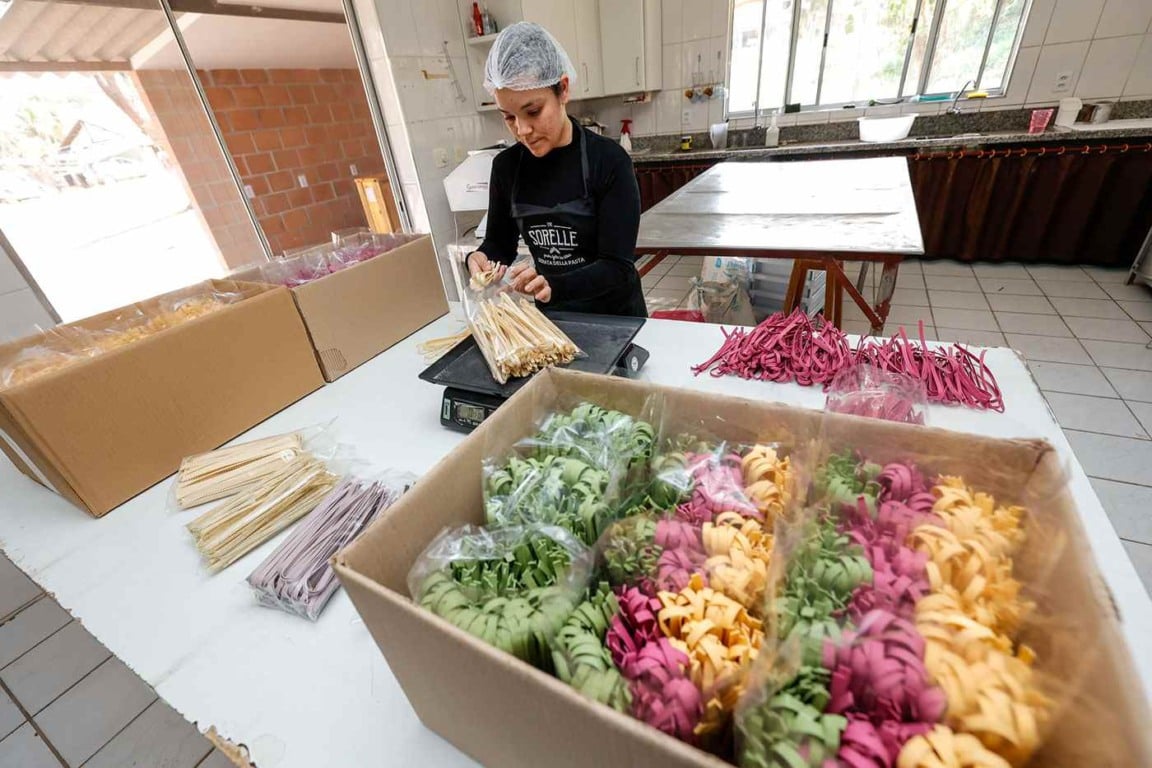 Mulher empacotando massas coloridas artesanais em fábrica local, representando o turismo rural e a tradição em Jundiaí.
