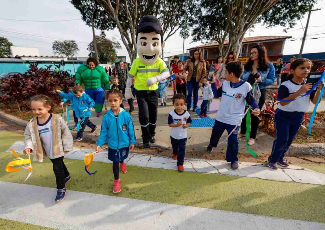 Crianças e adultos participam de uma atividade na Área da Infância em Jundiaí, acompanhadas por mascotes e segurando fitas coloridas.