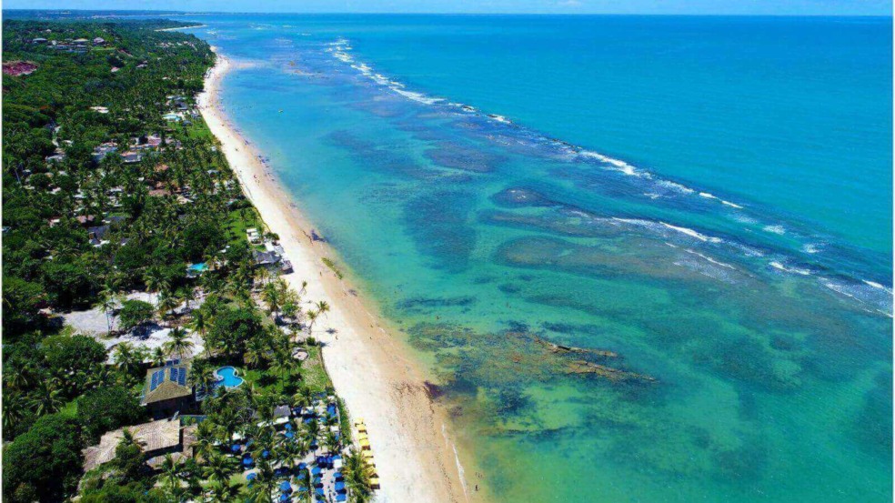 Praia paradisíaca em Trancoso, Bahia, com águas cristalinas, faixa de areia extensa e vegetação exuberante ao longo da costa. Praia paradisíaca em Trancoso, Bahia, com águas cristalinas, faixa de areia extensa e vegetação exuberante ao longo da costa.