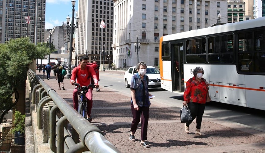 Pessoas andando em via com máscara