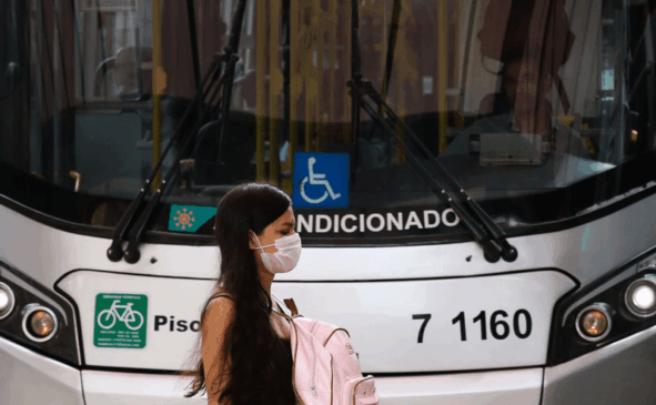 Mulher de máscara caminha em frente a ônibus