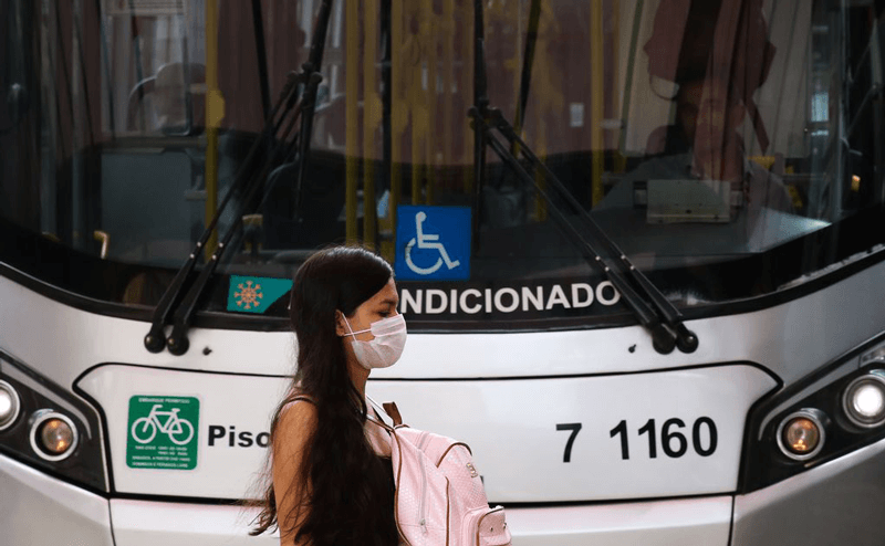 Mulher de máscara caminha em frente a ônibus
