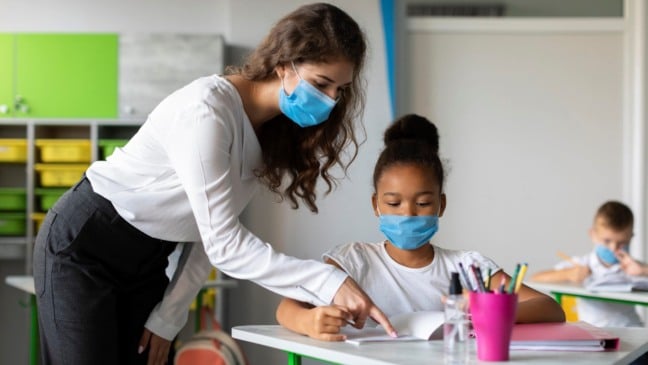 Professor com aluna de máscaras em sala de aula