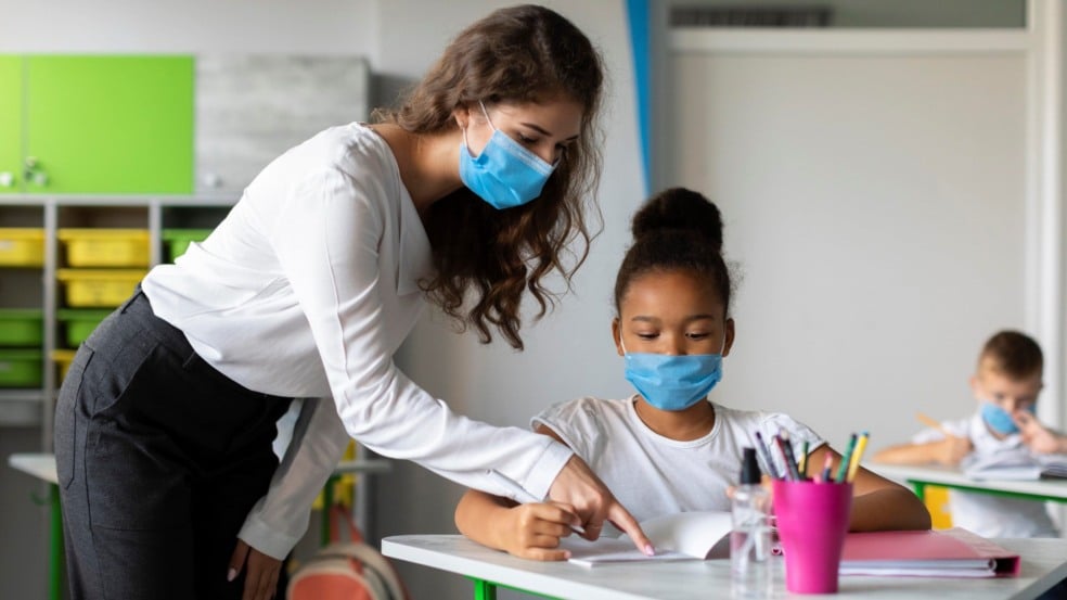 Professor com aluna de máscaras em sala de aula