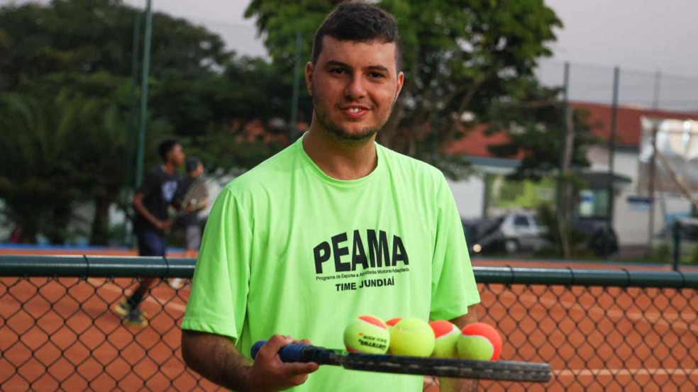 Atleta do PEAMA com camiseta verde segura raquete com bolinhas de tênis na quadra do Bolão, em Jundiaí.