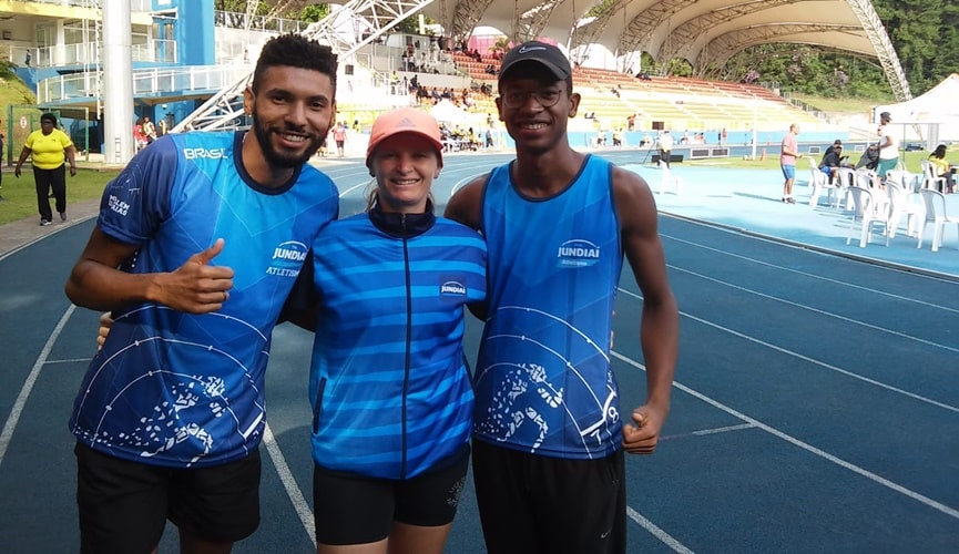 Homem de uniforme azul, à esquerda; mulher de uniforme azul ao centro; e rapaz de óculos com uniforme azul, à direita
