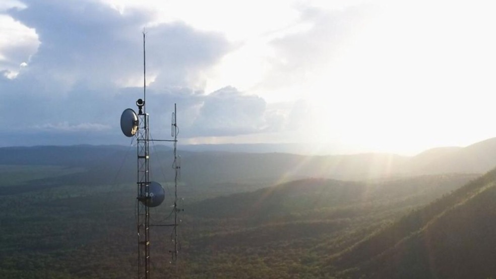 Torre de comunicação com antenas em um cenário montanhoso e ensolarado.