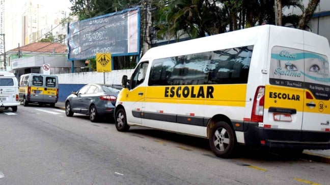 Vans de transporte escolar estacionadas em frente a uma escola em Jundiaí.