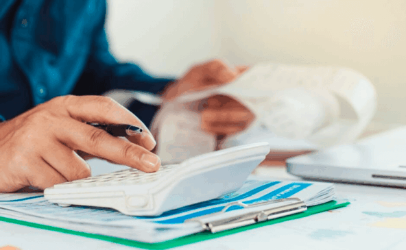 Homem usa calculadora e preenche papéis sobre a mesa