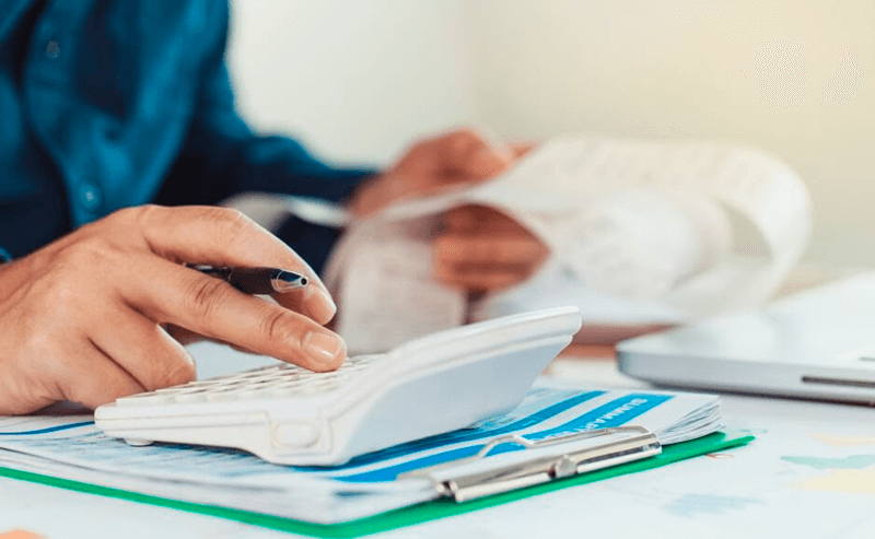 Homem usa calculadora e preenche papéis sobre a mesa