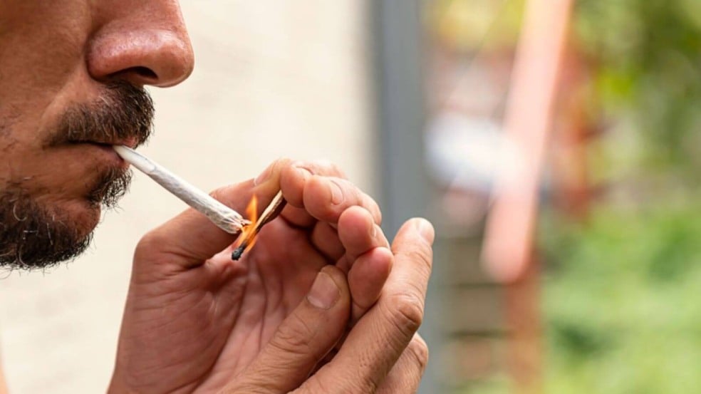 Homem acendendo um baseado de maconha ao ar livre, close-up no rosto e nas mãos, destacando o uso da substância.