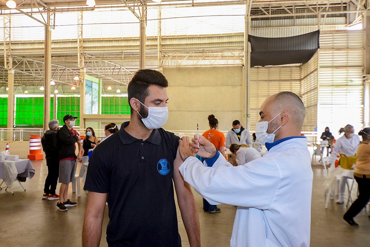 Homem sendo vacinado por um auxiliar da saúde