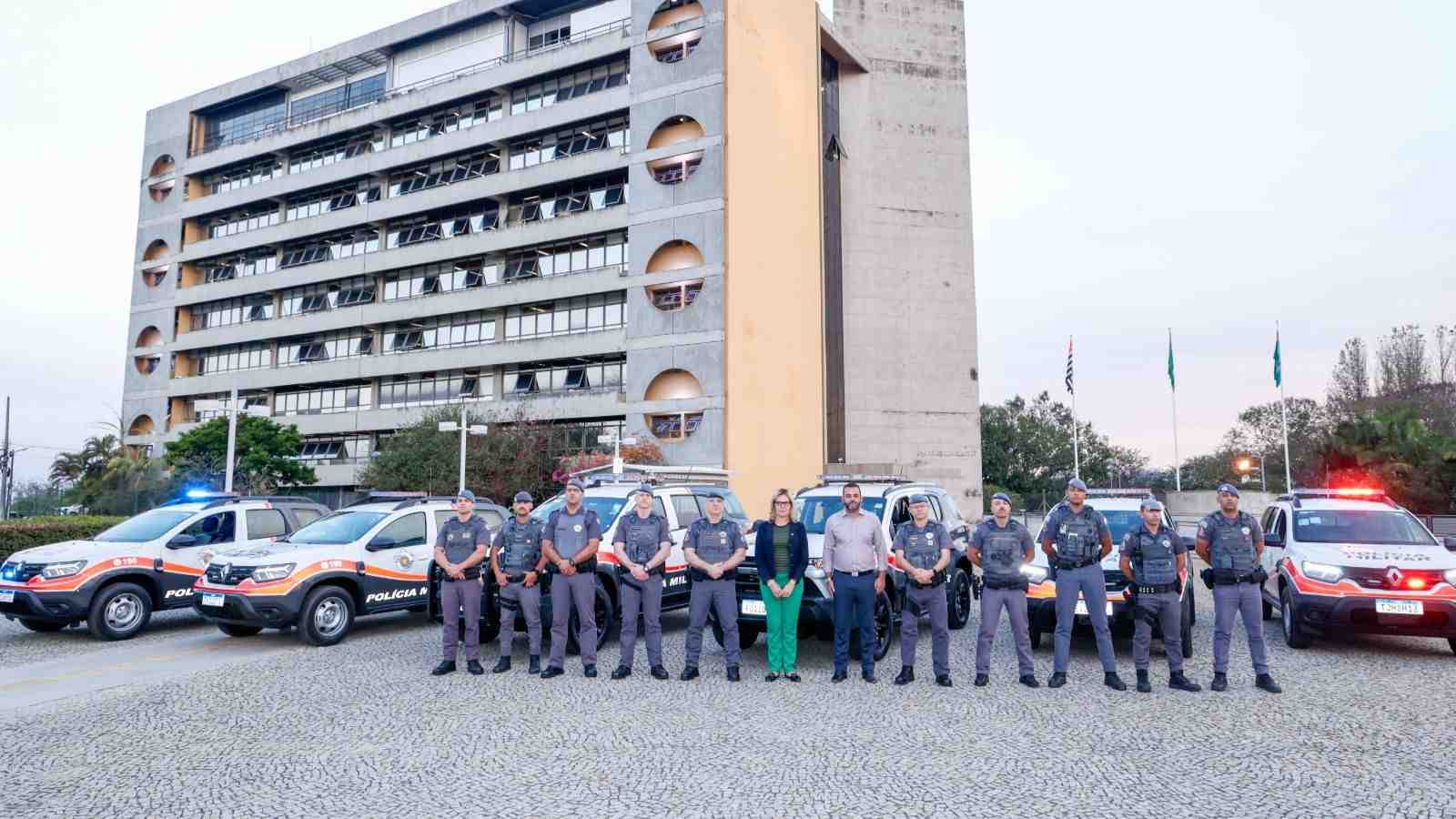 Policiais militares, prefeito Gustavo Martinelli e vereadora Carla Basílio posam em frente a viaturas novas da Polícia Militar, estacionadas em frente ao Paço Municipal de Jundiaí.