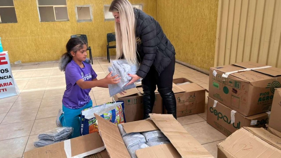 Voluntária entrega agasalhos novos para criança em ação social. Voluntária entrega agasalhos novos para criança em ação social.