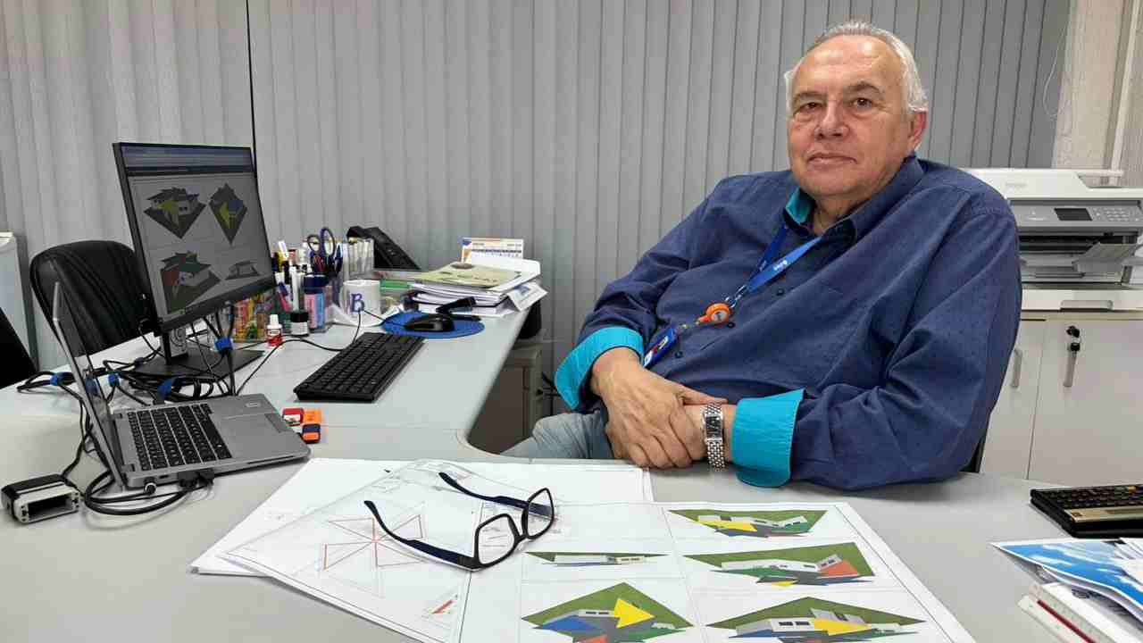 Engenheiro Walter da Costa e Silva trabalhando no projeto da Cidade das Crianças em Jundiaí, com desenhos e um computador em sua mesa de escritório.