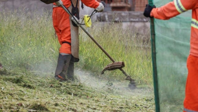 Zelador municipal utilizando roçadeira para cortar grama alta em bairro de Jundiaí. ‘Quem Ama, Cuida’