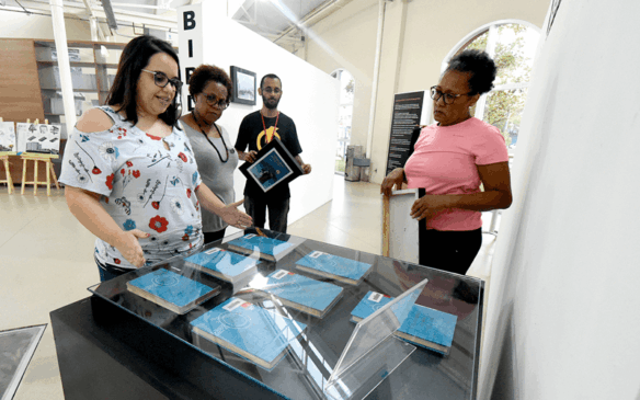 Quatro pessoas estão ao redor de uma câmara com livros de capa dura azul