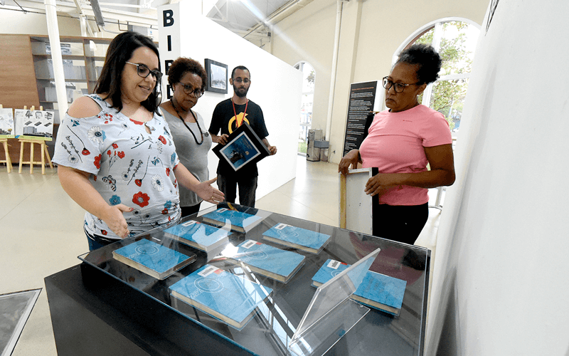 Quatro pessoas estão ao redor de uma câmara com livros de capa dura azul