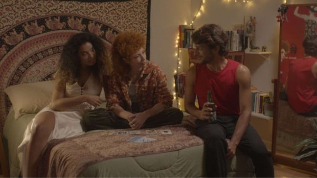 Três jovens sentados em um quarto aconchegante conversam sobre cartas de tarô espalhadas sobre a cama.