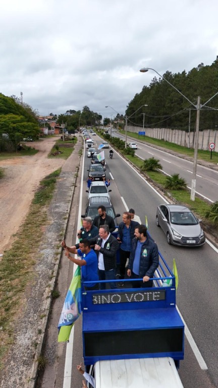 Parimoschi em cima de carro em carreata com apoiadores em Jundiaí, seguido por fila de veículos em avenida movimentada.