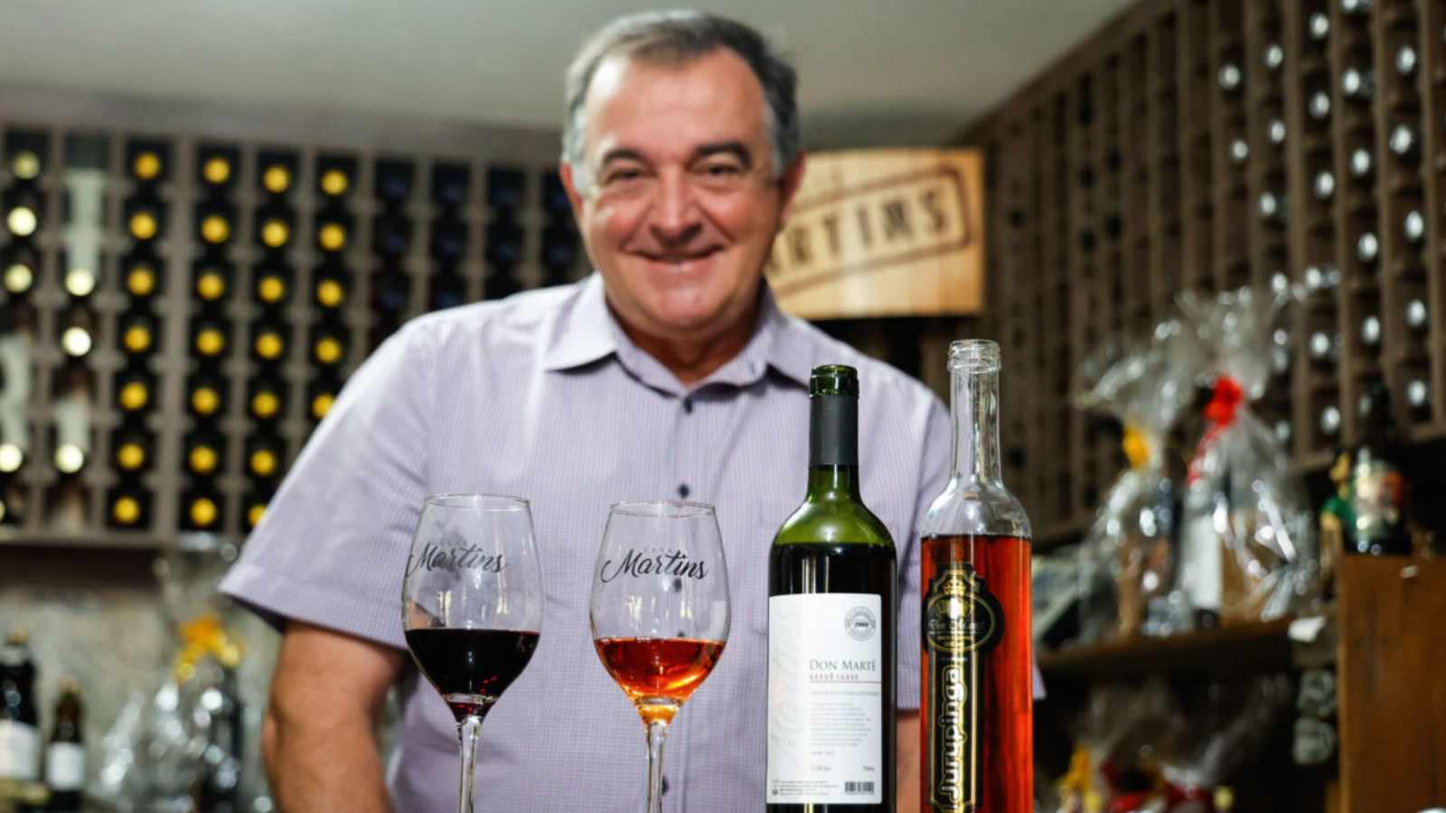 Proprietário da vinícola Martins com os vinhos premiados em frente à mesa.