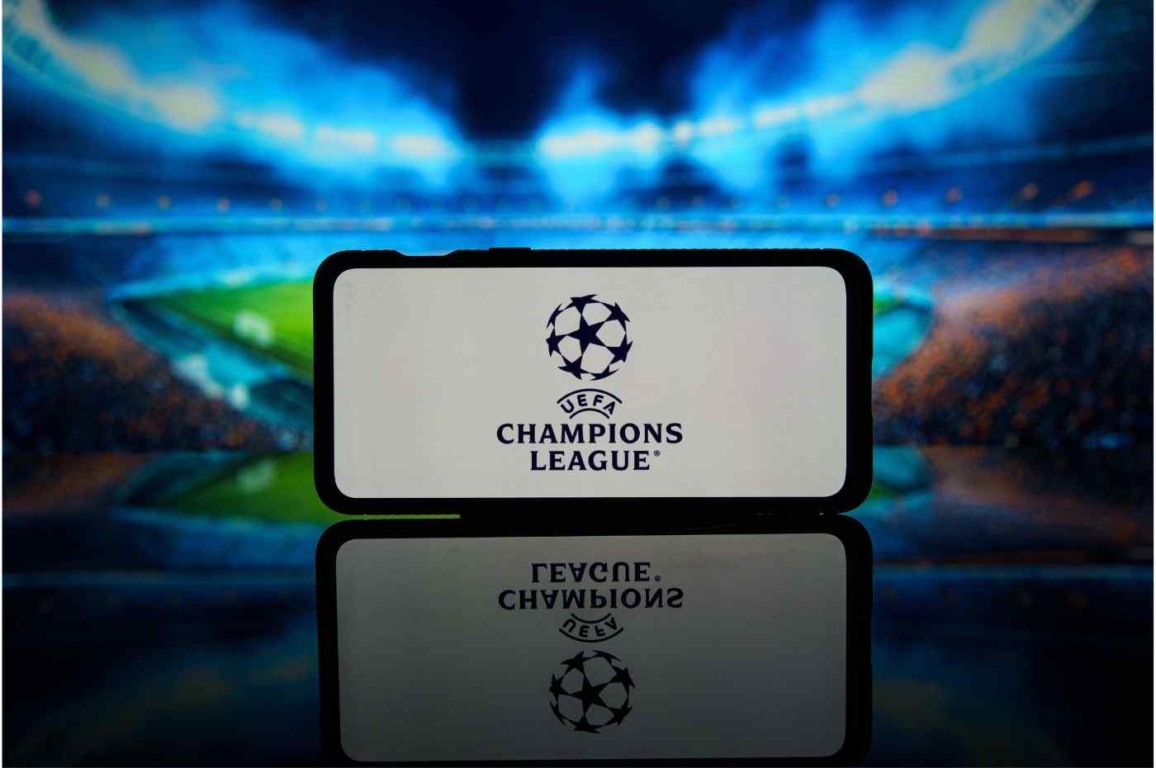 Logo da UEFA Champions League exibido em um smartphone, com estádio iluminado ao fundo.