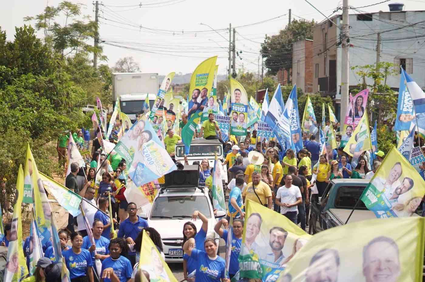 Caminhada de campanha de Parimoschi com apoiadores no Jardim Novo Horizonte, segurando bandeiras e cartazes em apoio ao candidato e seus aliados.