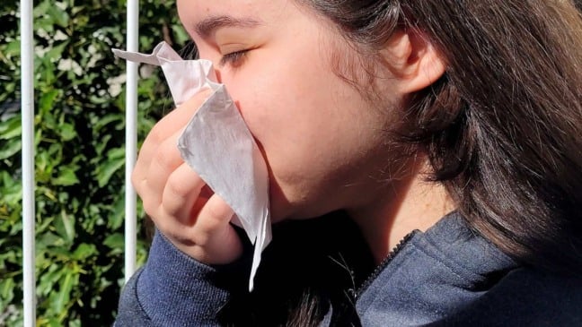 Garota assoando o nariz por alergia ao pólen das flores na Primavera