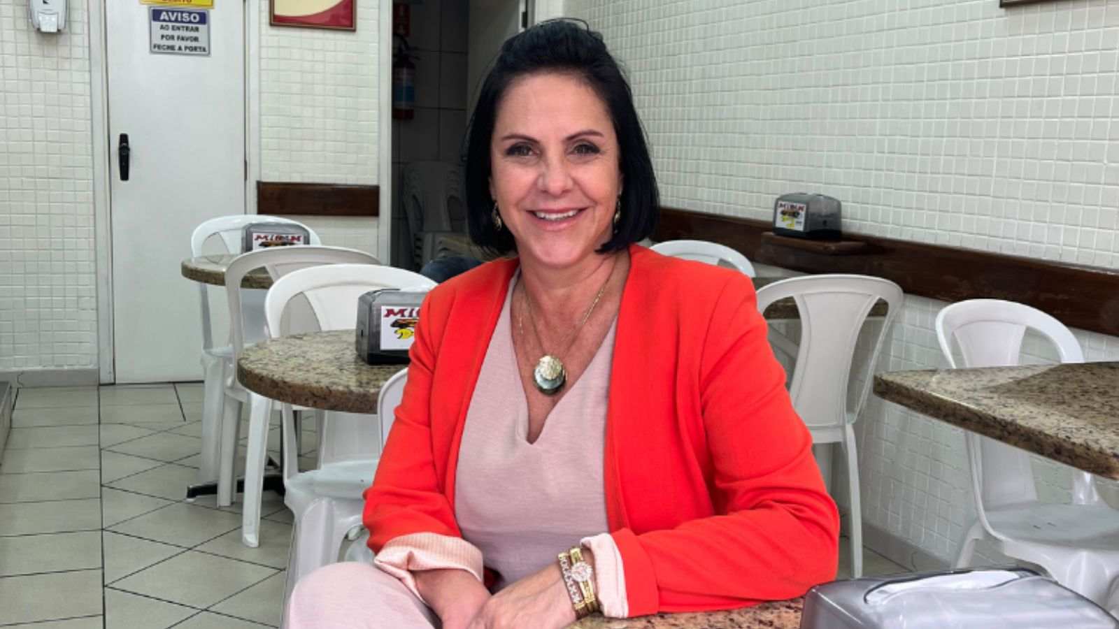 Leandra Maia, presidente da ACE Jundiaí, sentada em mesa de restaurante no Centro da cidade, usando blazer vermelho e blusa clara, sorrindo para a câmera.