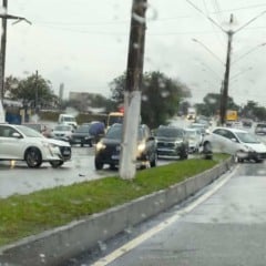 Agentes de trânsito controlam o fluxo de veículos em uma via movimentada sob chuva, após um acidente envolvendo dois carros brancos; um deles está atravessado na pista e o outro sobre o canteiro central. Agentes de trânsito controlam o fluxo de veículos em uma via movimentada sob chuva, após um acidente envolvendo dois carros brancos; um deles está atravessado na pista e o outro sobre o canteiro central.
