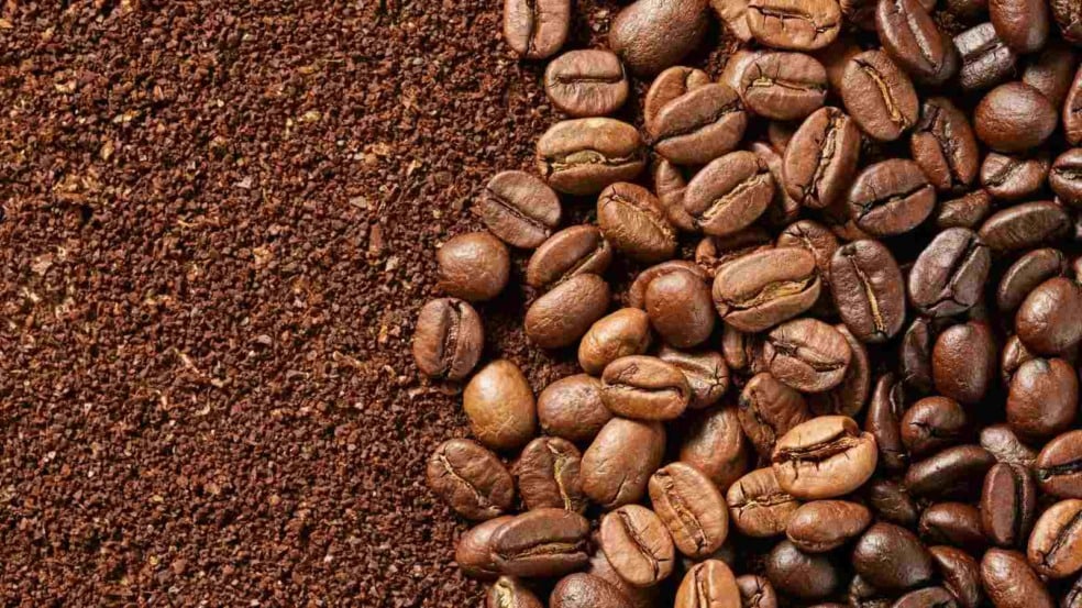 Grãos de café torrado ao lado de café moído em close-up.