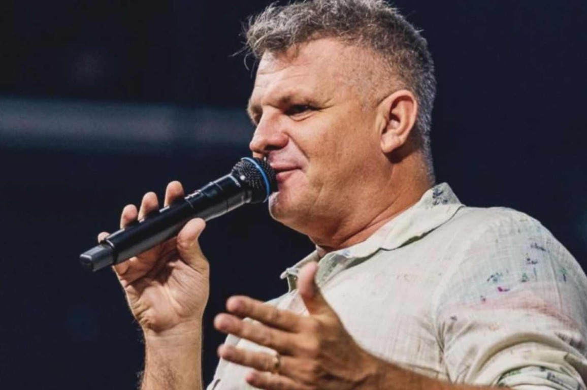 Apóstolo Rina, fundador da igreja Bola de Neve, segurando microfone enquanto fala em evento religioso, usando camisa clara Apóstolo Rina, fundador da igreja Bola de Neve, segurando microfone enquanto fala em evento religioso, usando camisa clara