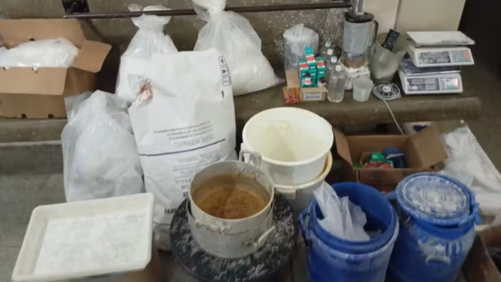 Materiais apreendidos em Várzea Paulista, incluindo sacos de pó, baldes, panelas, balanças de precisão, liquidificador e frascos usados na produção de drogas e bebidas falsificadas.