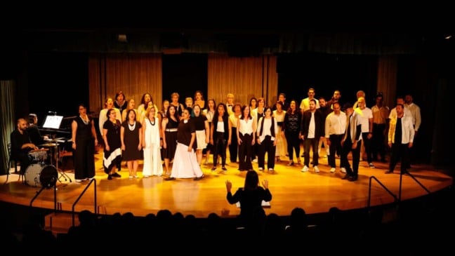 Apresentação de coral em Jundiaí com regente, cantores e músicos no palco de teatro.