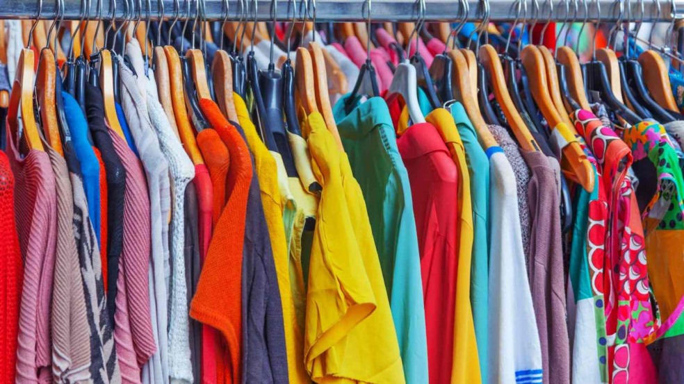 Roupas coloridas penduradas em cabides em arara de bazar beneficente.