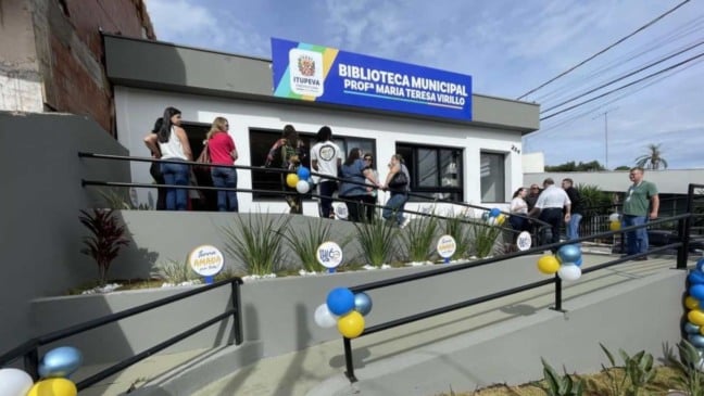 Fachada da nova Biblioteca Municipal Prof.ª Maria Teresa Virillo, em Itupeva, com pessoas na entrada e decoração com balões coloridos. Fachada da nova Biblioteca Municipal Prof.ª Maria Teresa Virillo, em Itupeva, com pessoas na entrada e decoração com balões coloridos.