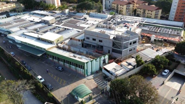 Vista aérea do Hospital Universitário de Jundiaí, com blocos hospitalares, área em obras e prédios residenciais ao fundo.