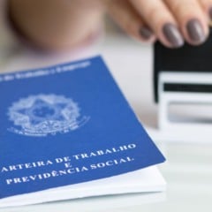Carteira de Trabalho e Previdência Social ao lado de uma pessoa carimbando documento em mesa, simbolizando contratação formal.