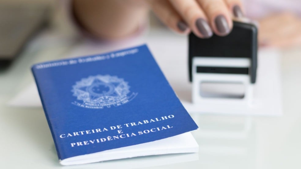 Carteira de Trabalho e Previdência Social ao lado de uma pessoa carimbando documento em mesa, simbolizando contratação formal.
