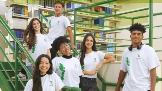 Estudantes do IFSP posando em escada no campus, com camisetas do Instituto Federal e biblioteca ao fundo.