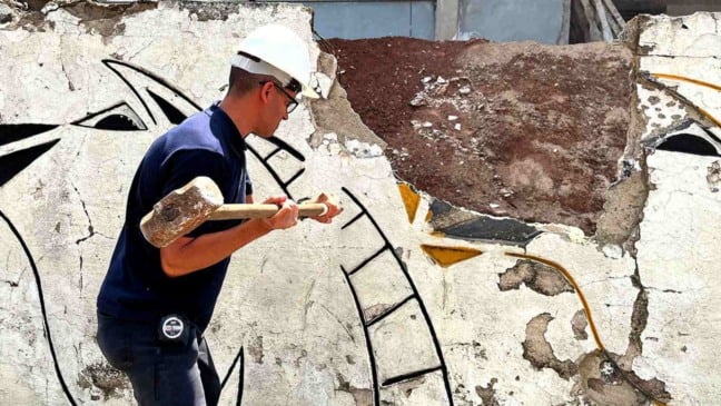 Homem com capacete branco derruba muro com marreta durante obra do novo Hospital Municipal de Várzea Paulista.