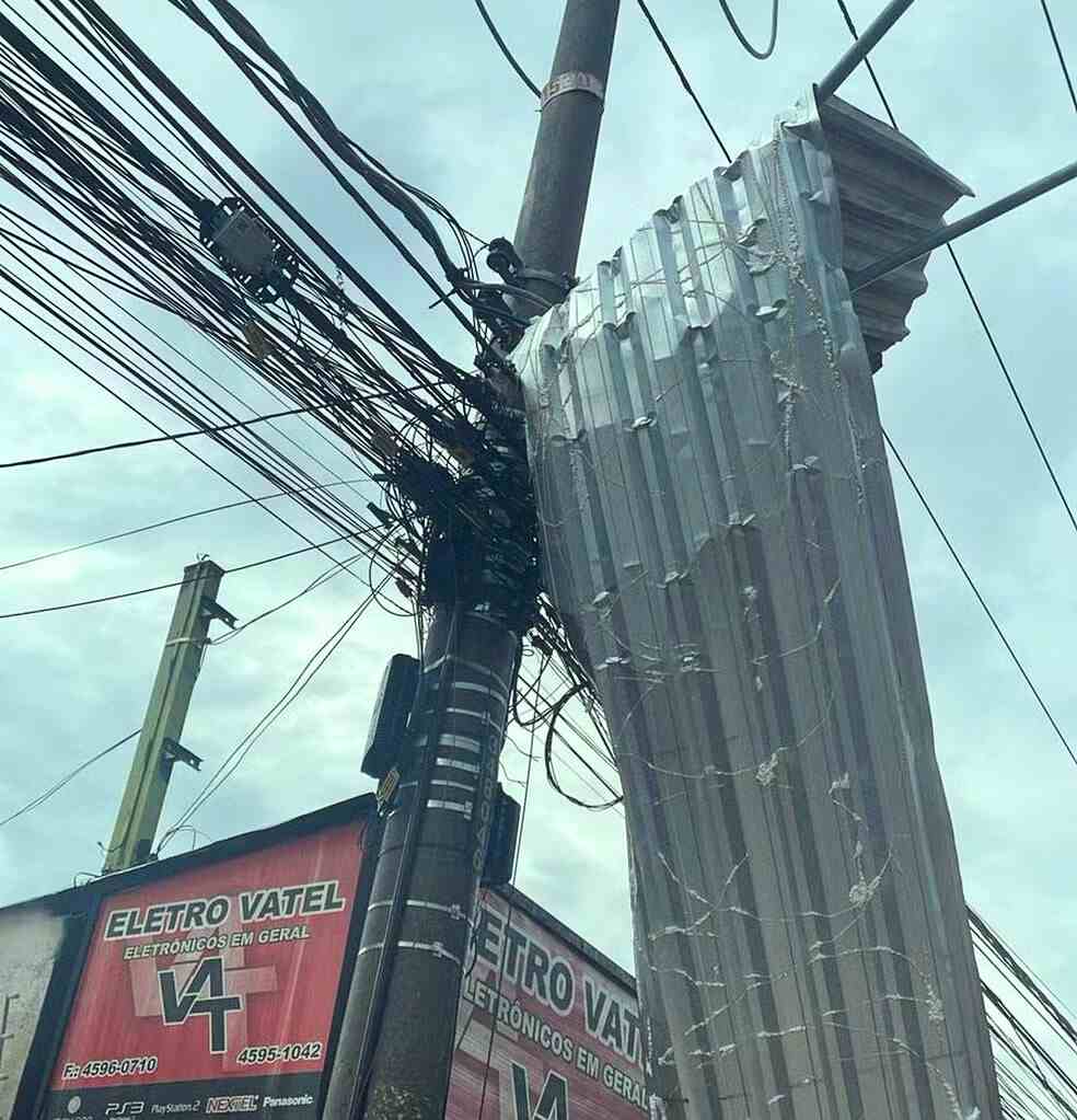 Ventos fortes em Várzea Paulista causam destelhamento; telha de metal fica presa em poste, danificando fiações elétricas.